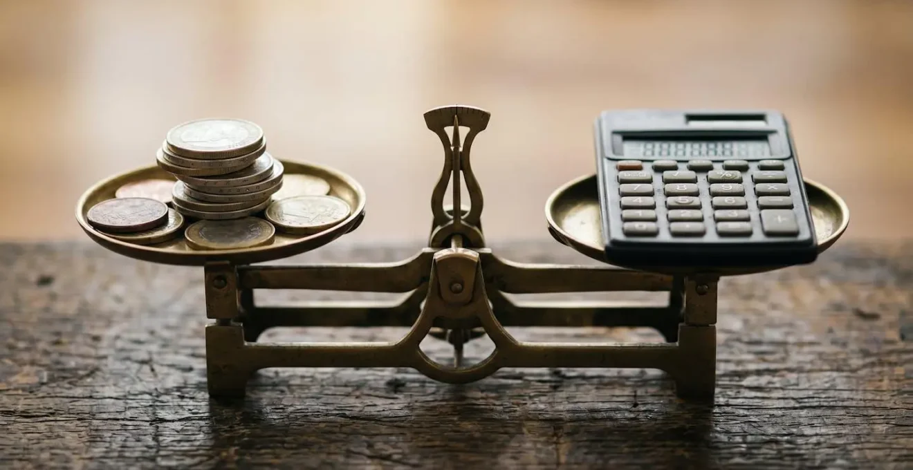 Gros plan macro sur une calculatrice et des pièces de monnaie en équilibre, symbolisant l'arbitrage financier entre payer de sa poche et déclarer un sinistre