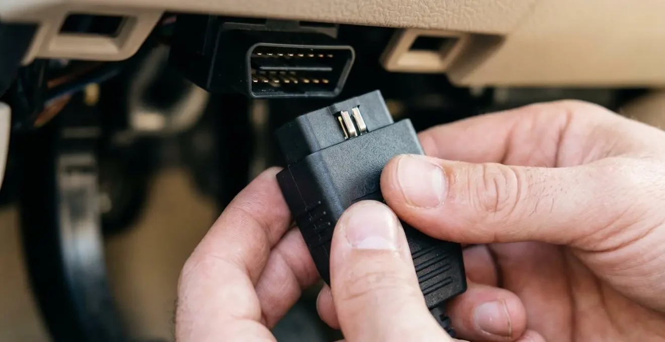 Gros plan de mains tenant un boîtier de diagnostic OBD2 compact lors de la connexion à la prise automobile