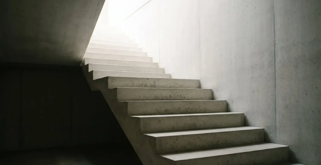 Escalier architectural éclairé progressivement symbolisant la remontée du coefficient bonus après un malus, métaphore du parcours patient vers le bonus 50