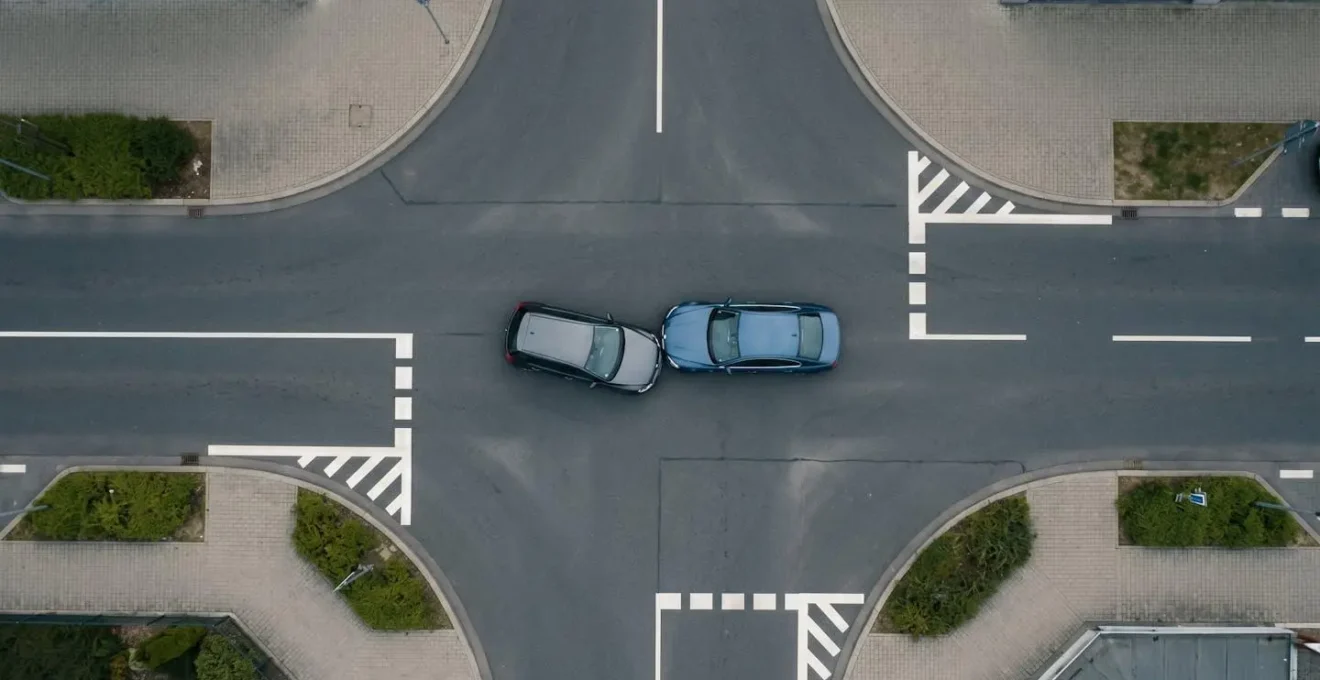 Vue en plongée minimaliste d'une intersection urbaine après un accident, deux véhicules positionnés avec espace négatif, symbolisant l'importance du croquis précis sur le constat